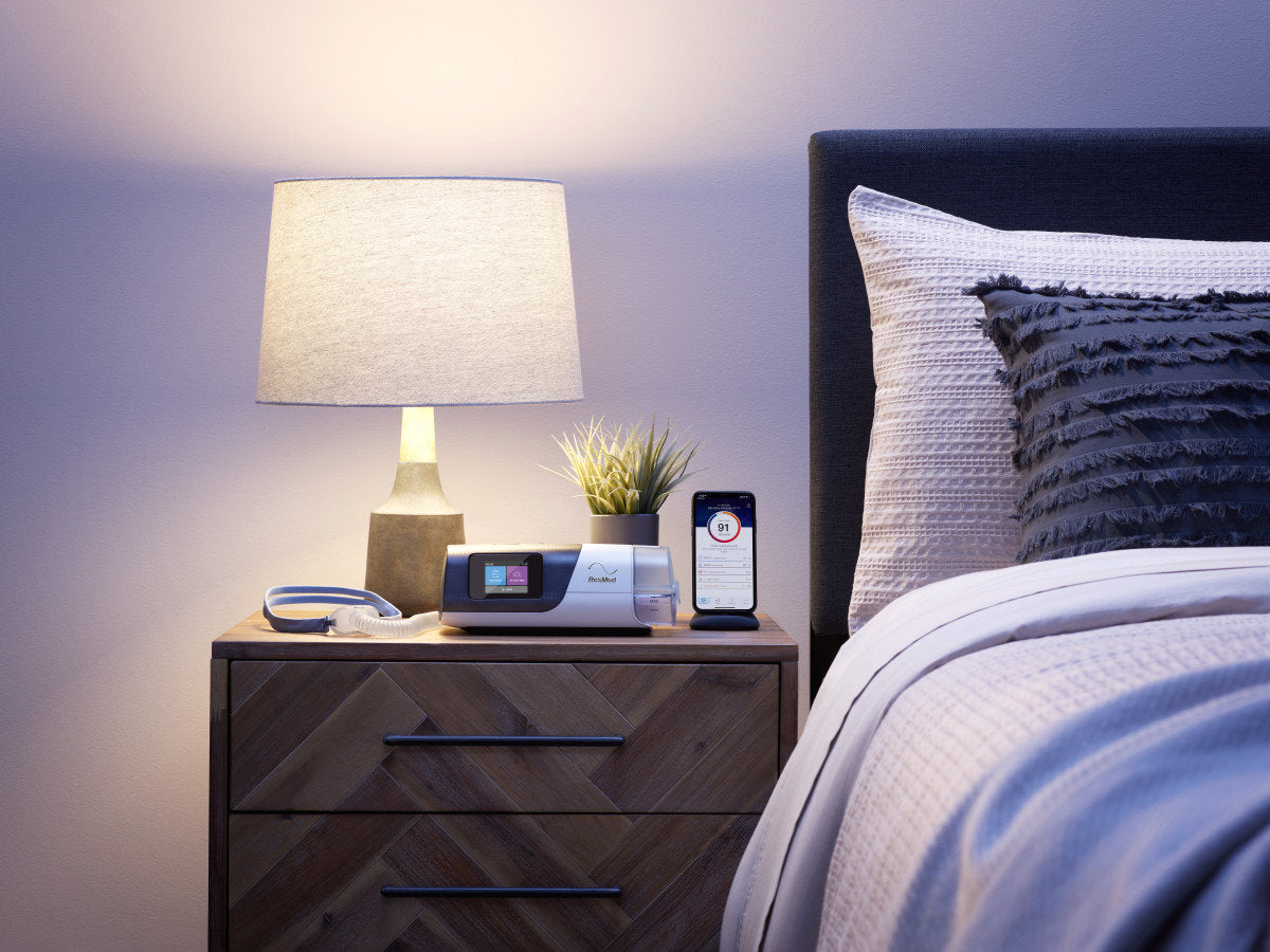 ResMed AirSense 11 placed on a nightstand in front of lamp